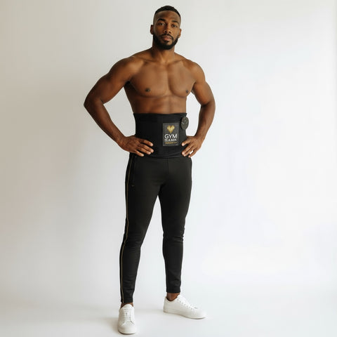 Male model standing and wearing a black GYM IN A BOX® StimFitBelt around his waist, styled with black athletic pants against a white background.